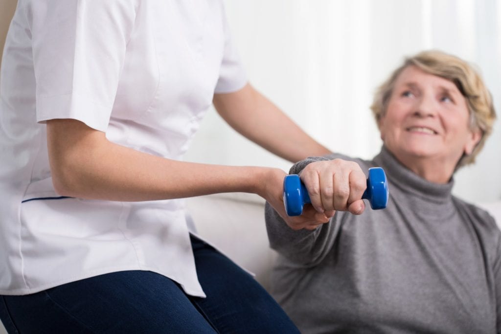 Aged exercising woman and female physiotherapist's help