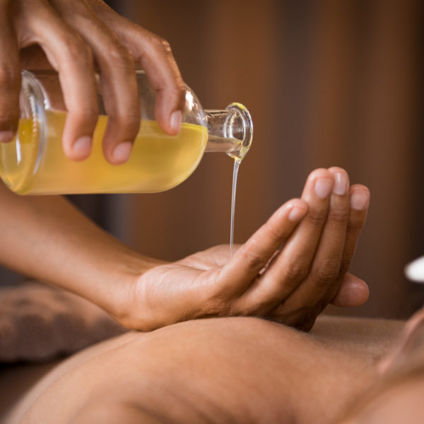 Closeup of masseur hands pouring aroma oil on woman back. Masseuse prepare to do oriental spa procedure for relaxing treatment. Therapist doing aromatherapy oil massage on woman body.