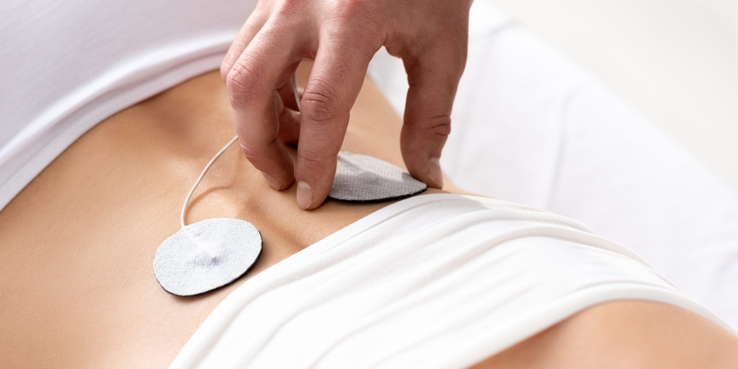 Cropped view of therapist setting electrode on patient back during electrode treatment on grey background